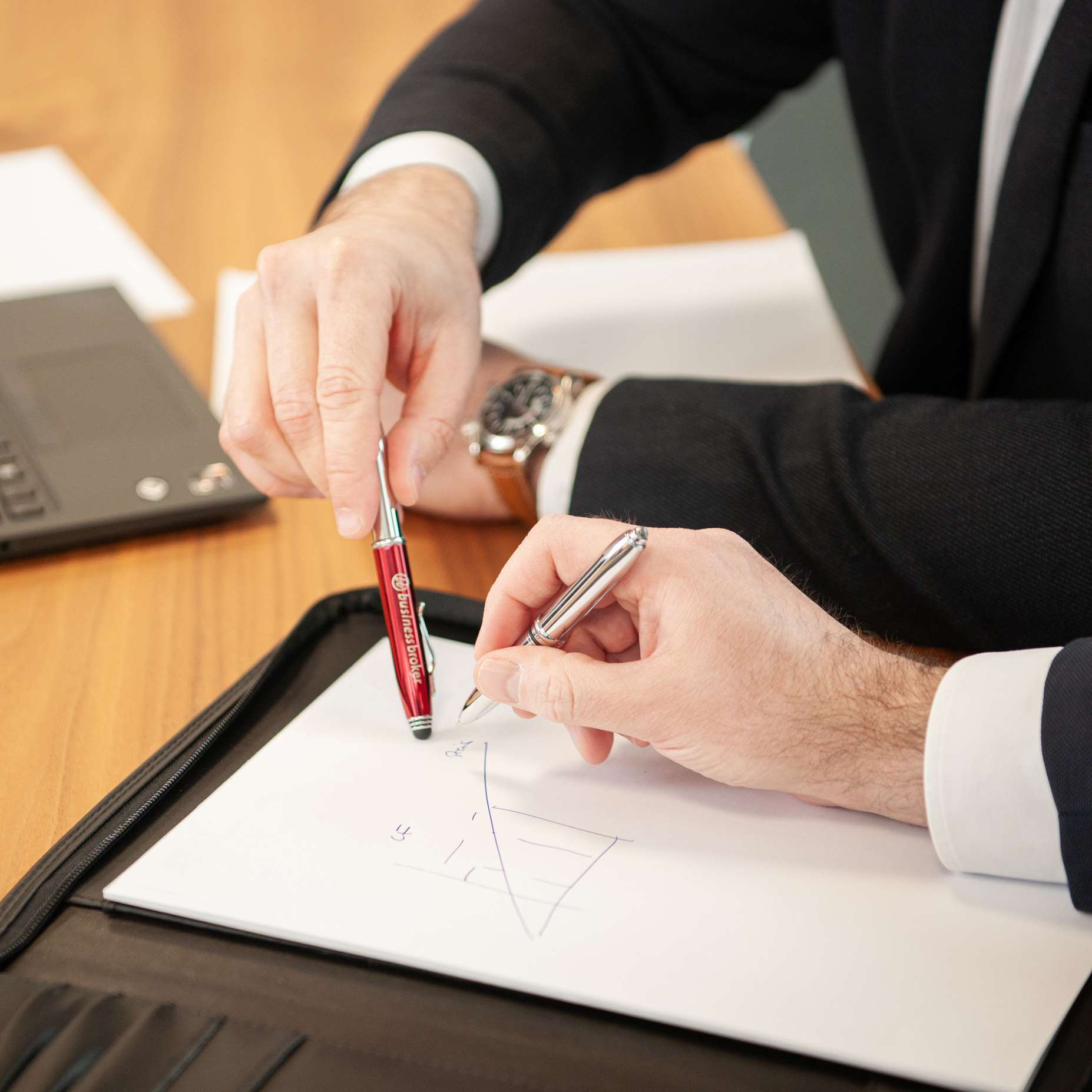 Zwei Hände von Business Broker Mitarbeitern, die eine Skizze auf Papier besprechen